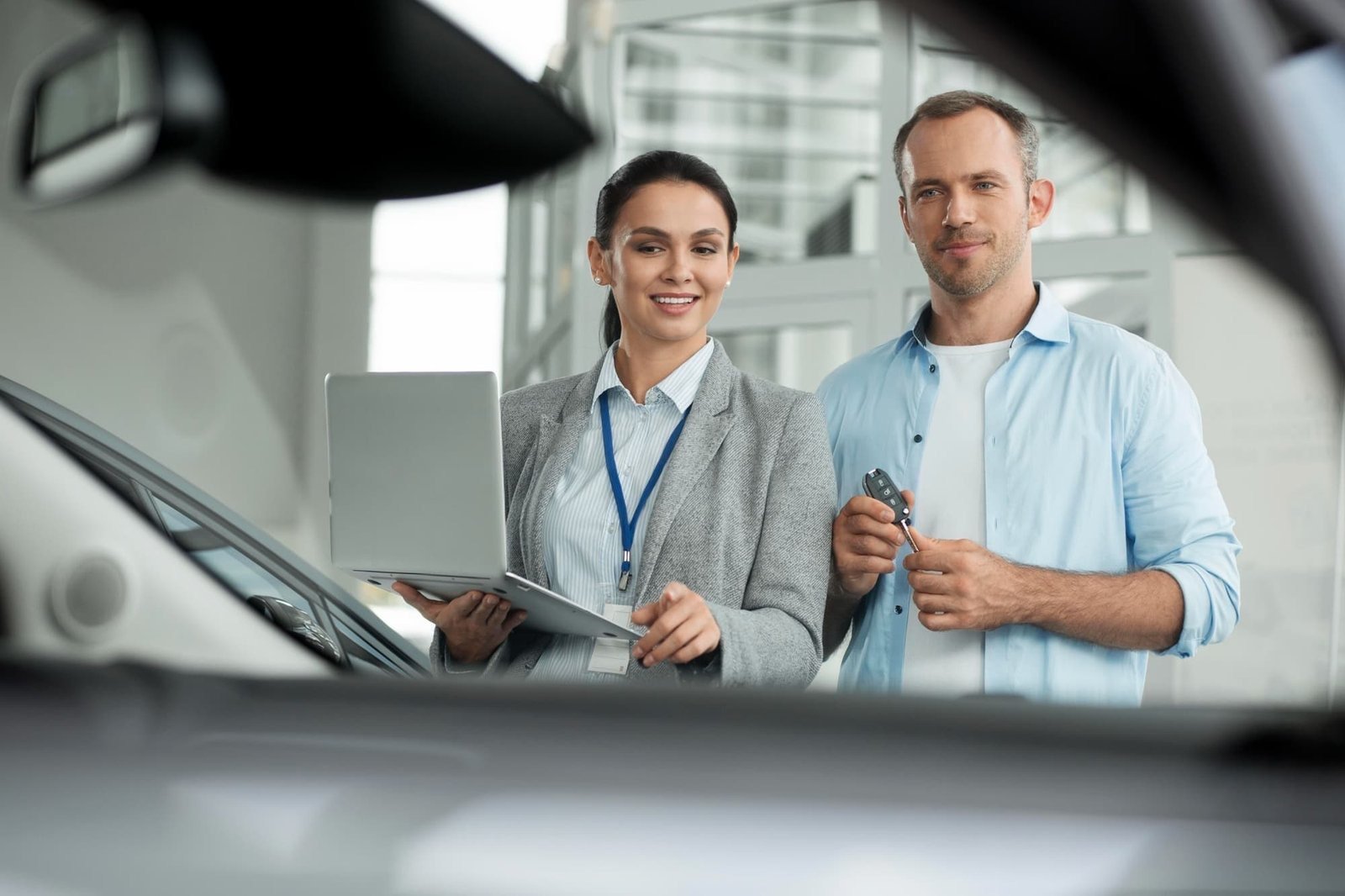 Two dealership staff with a laptop and car keys, seen over a car bonnet