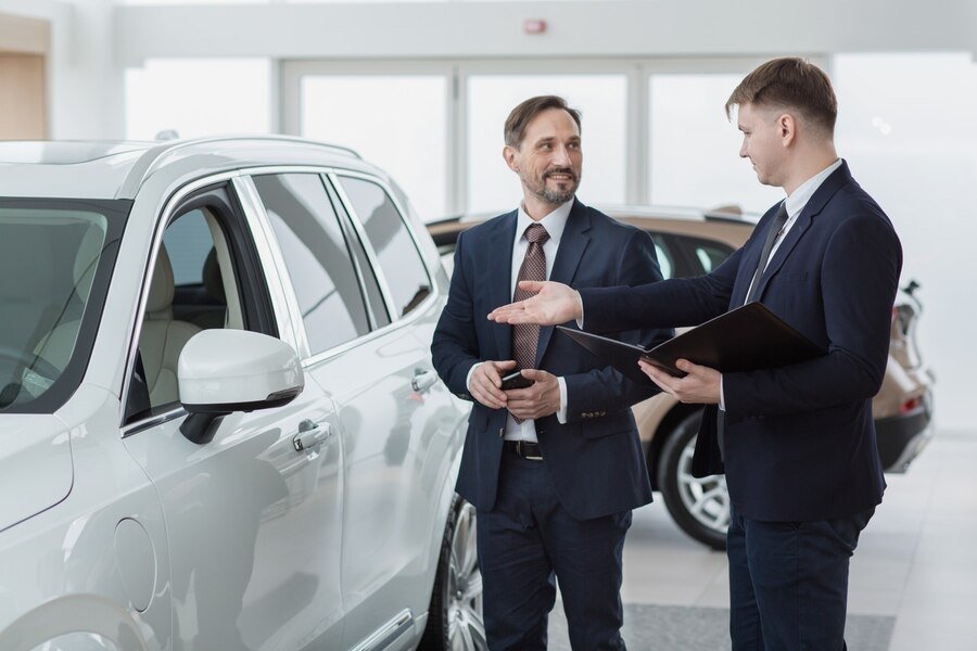 Two dealership staff talking beside a white SUV in a showroom